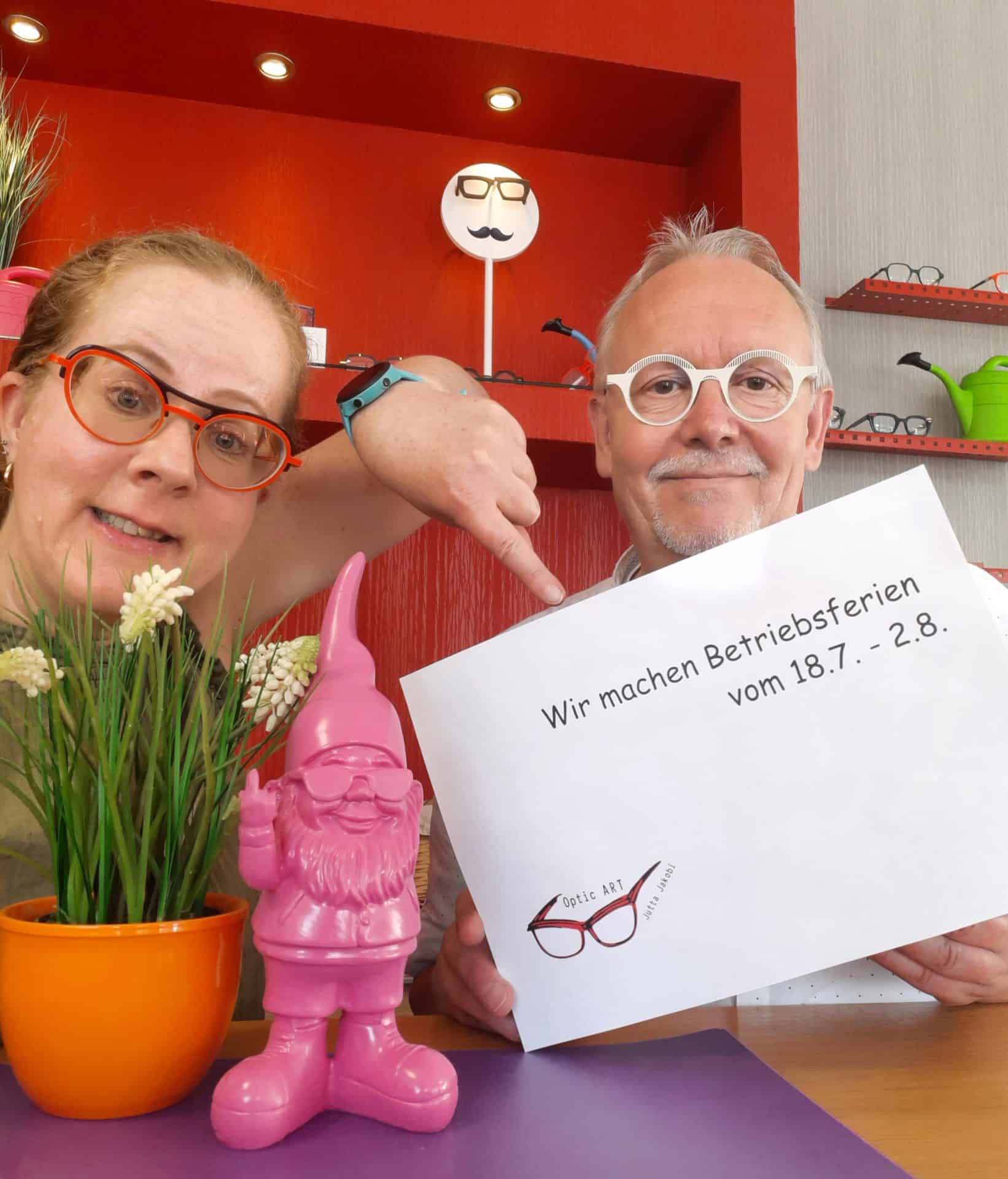 Optikerteam mit Schild zu Betriebsferien im Geschäft